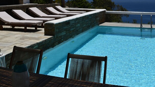 Un espace aménagé au bord de la piscine, avec des chaises longues, une table et une vue sur l’océan.