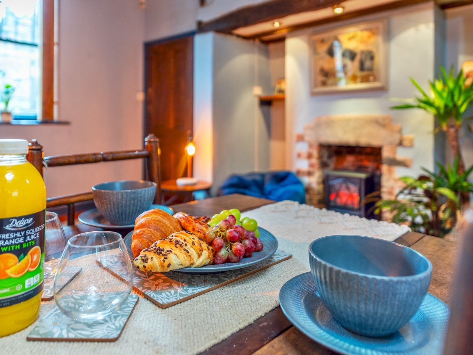 A breakfast setting with croissants, grapes, and a bottle of orange juice on a table.