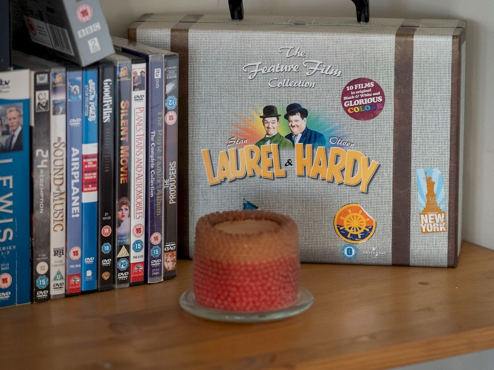Una colección de DVDs titulada "The Feature Film Collection" de Laurel & Hardy, con un reproductor de DVD y un pastel sobre una mesa.