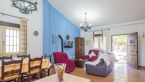 Una sala de estar con pared azul, muebles de madera, una araña y un comedor con sillas y una mesa.