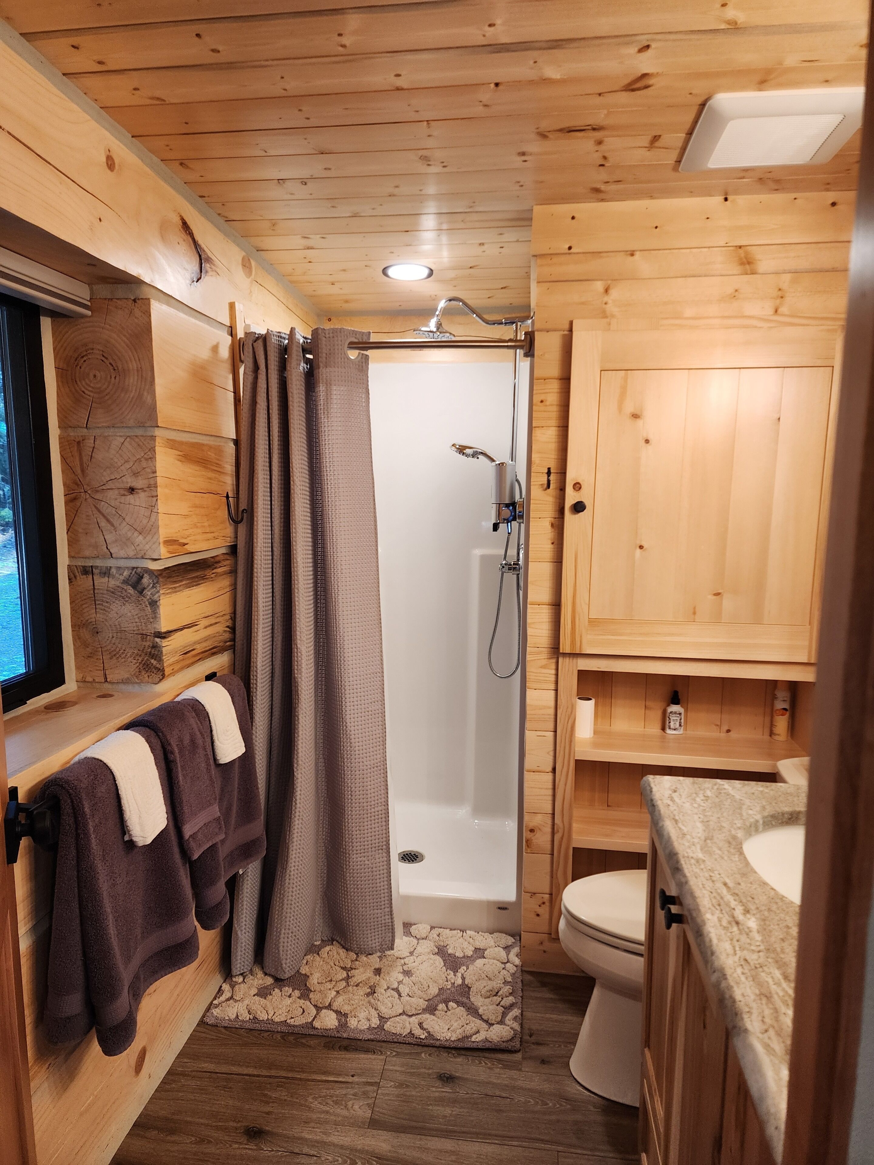 A wooden cabin bathroom with a shower, toilet, and a sink area.