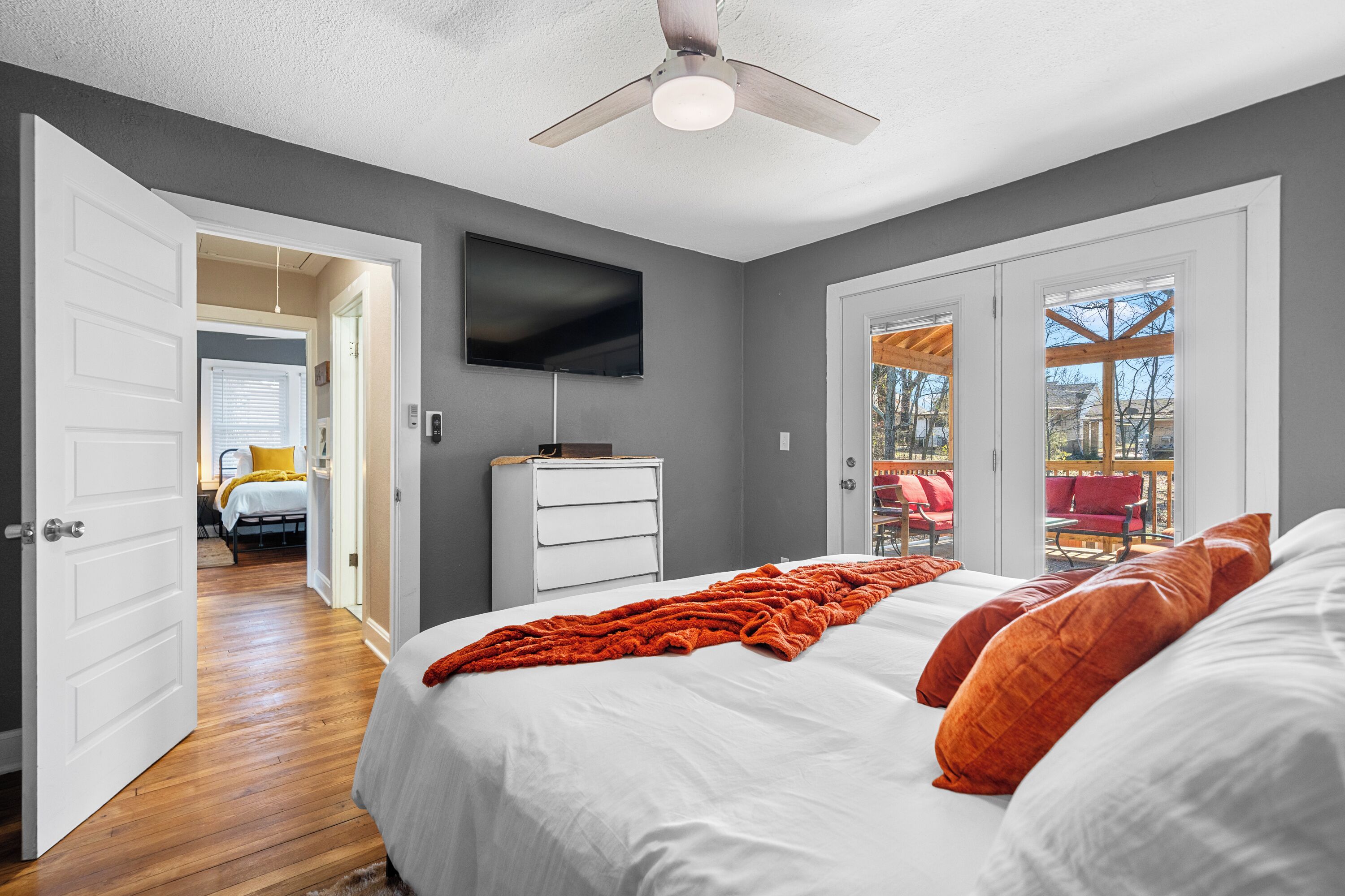 A bedroom with a bed, a flat-screen TV, a ceiling fan, and a sliding glass door leading to an outdoor area.