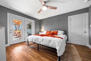 Quarto com cama, ventoinha no teto e vista para um pátio exterior através de uma porta de vidro.