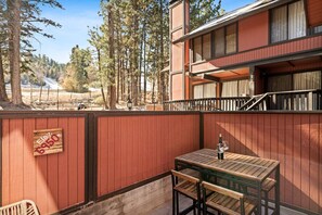 A wooden table with a bottle, a chair, and a sign reading "Flex 650" on a balcony with a view of trees and a building. - Summit Slope Side + Steps 2 Slopes! (Big Bear Lake)
