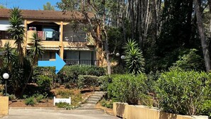 Un edificio de dos pisos con balcón, rodeado de exuberante follaje y árboles.