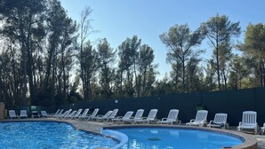 Una piscina con sillas de descanso, rodeada de árboles.