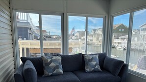 A dark blue sofa with geometric patterned cushions in a room with large windows overlooking a marina and residential buildings. - Waterfront Family Retreat with Dock, Kayaks & Beach Passes! (Stafford Township)