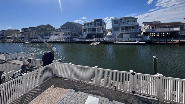 A waterfront property with a dock, a white fence, and a row of houses with balconies. - Waterfront Family Retreat with Dock, Kayaks & Beach Passes! (Stafford Township)