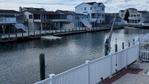 A waterfront property with a dock, a white fence, and a row of houses. - Waterfront Family Retreat with Dock, Kayaks & Beach Passes! (Stafford Township)