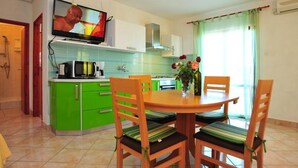Eine kompakte Küche mit grünen Schränken, einem Esstisch mit vier Stühlen, einem über der Arbeitsfläche montierten Fernseher und einer Vase mit Blumen auf dem Tisch.
