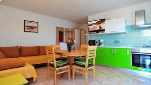 Ein gemütlicher Wohnbereich mit Sofa, Esstisch, Stühlen, einer Küchenzeile mit Herd und einem Fernseher.
