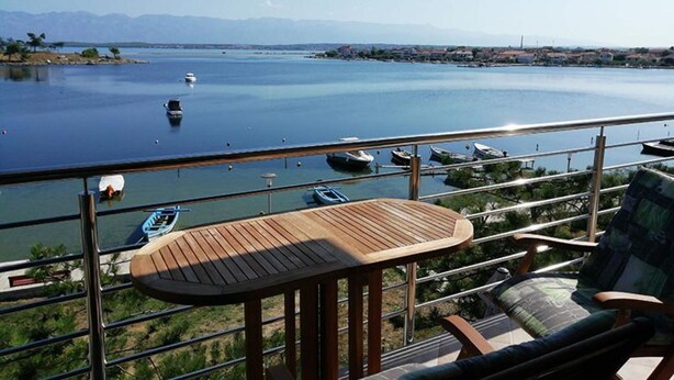 A balcony with a wooden table and chairs overlooking a calm body of water with boats.