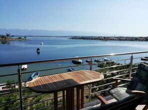 A balcony with a wooden table and chairs overlooking a calm body of water with boats. - Guest House Burela - One Bedroom Apartment with Balcony and Sea View (Nin)