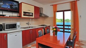 A compact kitchen with a TV, microwave, and sink. There's a dining table with chairs and a view of a body of water through a window.
