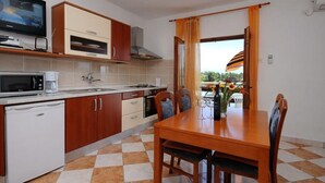 A compact kitchen with a microwave, coffee maker, and a small refrigerator. There is a dining table with chairs and a view of the outdoors through a window.