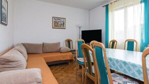 Una sala de estar acogedora con un sofá, una mesa de comedor con sillas, un televisor de pantalla plana y un cuadro en la pared.