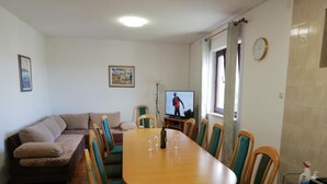 Un área de comedor con una mesa y sillas de madera, un sofá, un televisor y una ventana con cortinas.