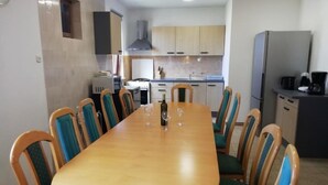 Un comedor con mesa y sillas de madera, una cocina al fondo y un refrigerador a la derecha.