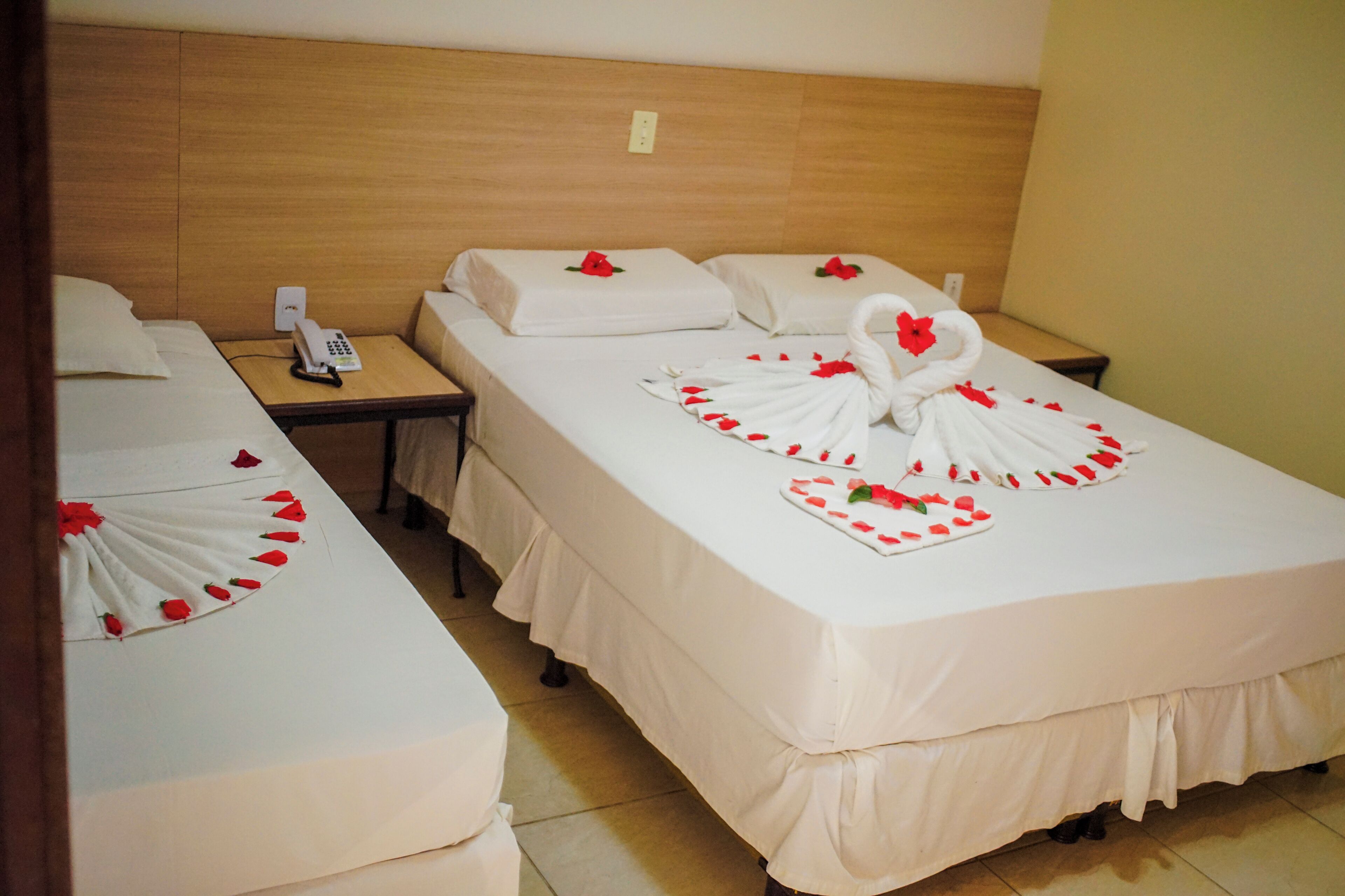 A hotel room with two beds, each with white linens and rose petals arranged on the beds. There is a telephone on the nightstand next to one bed.