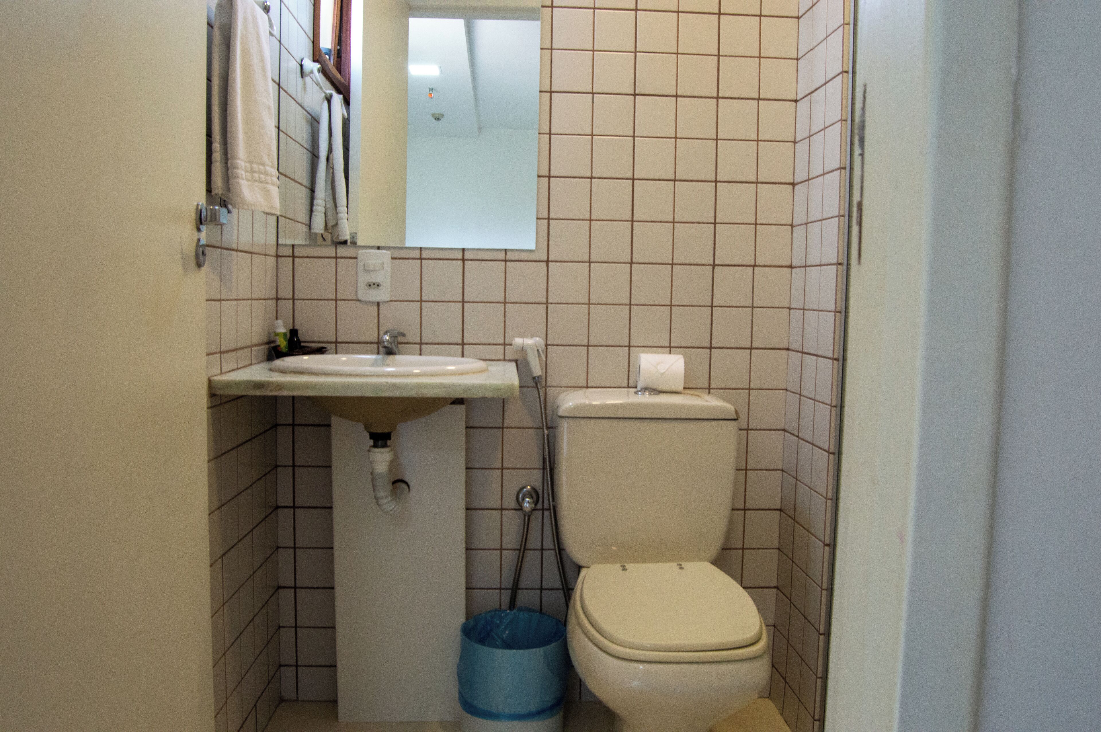 Et lille badeværelse med vask, toilet og blå skraldespand.