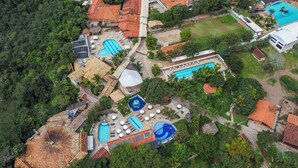 An aerial view of a resort with multiple swimming pools, a large covered area, and lush greenery. - Vila Velluti Hotel SPA (Gama)