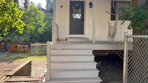 A wooden house with a front porch, a door with a wreath, and a small garden area with a hammock and a fence. - The Hikers Haven  (Thompson Falls)