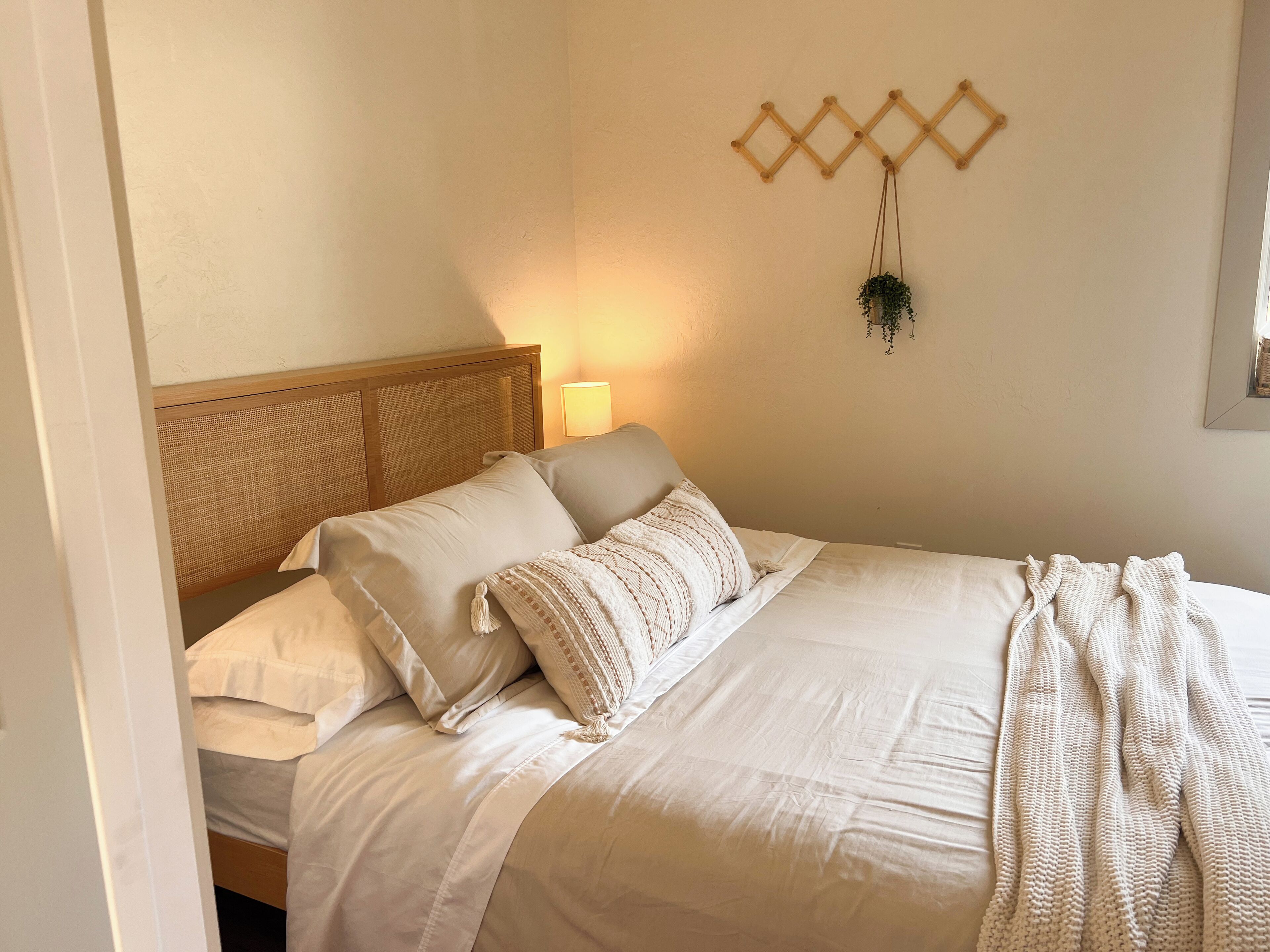 Una cama bien tendida con cabecera de madera, un adorno en la pared y una lámpara de noche.