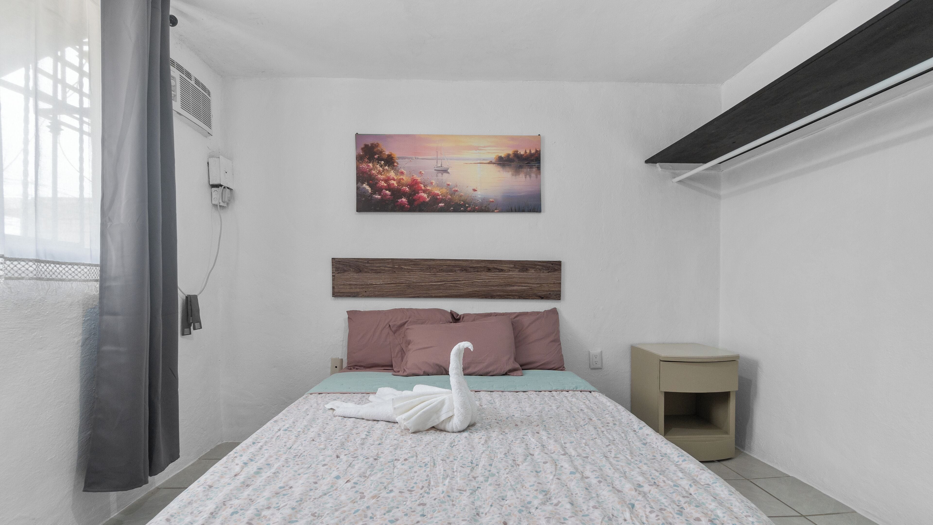 A bedroom with a bed, a painting, a wooden headboard, a nightstand, and a window with curtains.