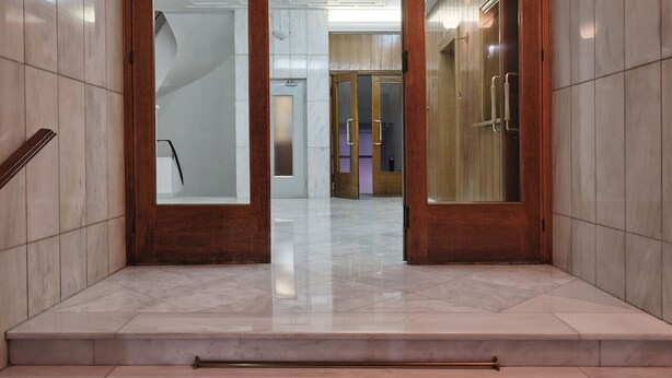 A modern lobby with marble flooring, wooden doors, and a glass elevator. - Anaktora Gardens Apt (Athina)