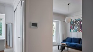 A modern living room with a blue sofa, a small round table, and a hanging light fixture. - Anaktora Gardens Apt (Athina)