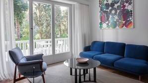 A living room with a blue sofa, a chair, a coffee table, and a colorful abstract painting on the wall. - Anaktora Gardens Apt (Athina)