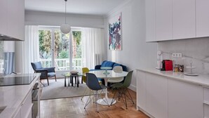 A modern kitchen and dining area with a large window, white cabinets, and a dining table with chairs. - Anaktora Gardens Apt (Athina)
