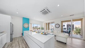 Una cocina moderna con una isla central, un área de comedor con un sofá blanco y vistas al exterior.
