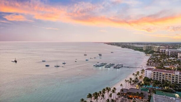 Un paisaje urbano costero con un puerto deportivo, hoteles frente a la playa y una vista despejada del océano.