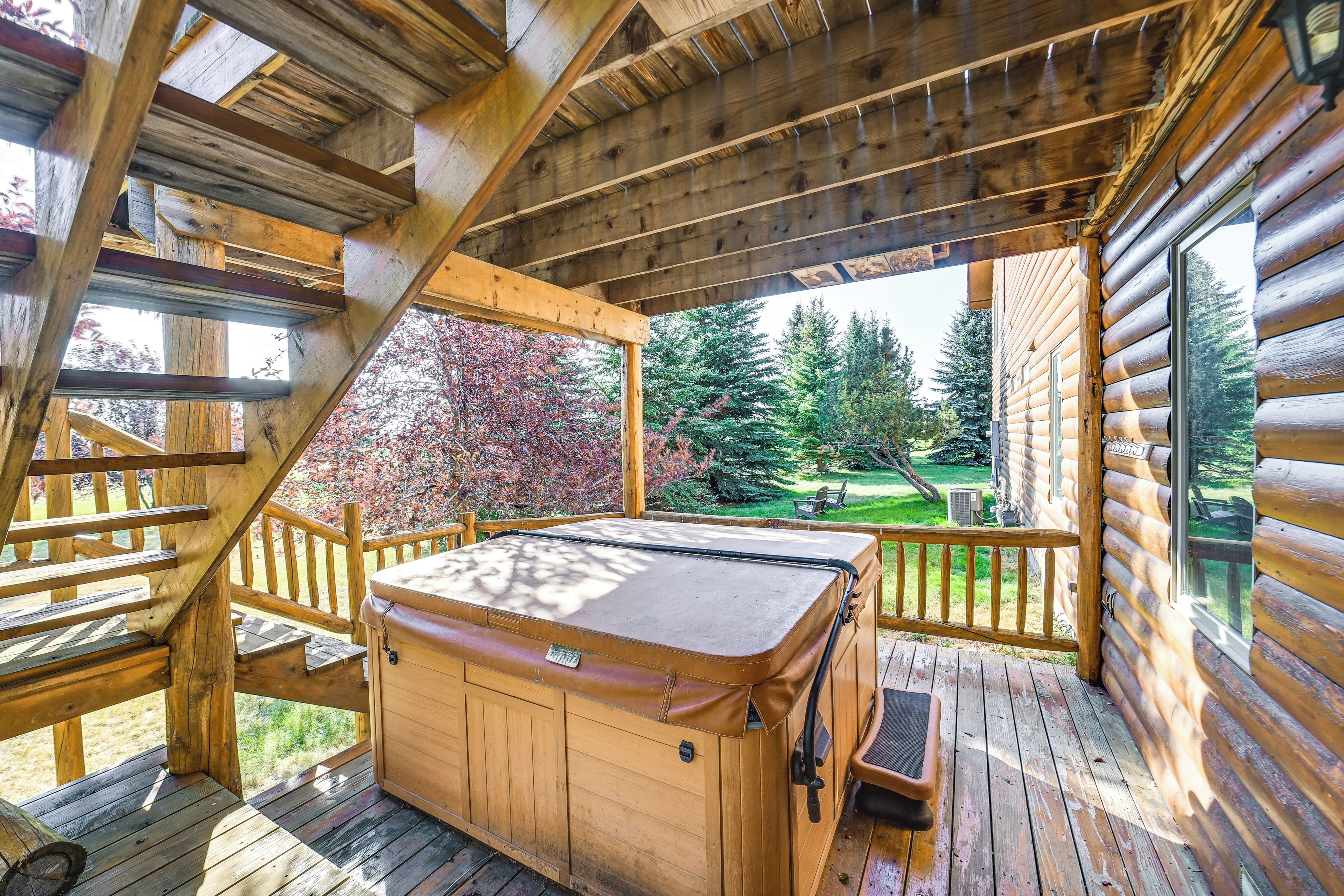 Eine Holzterrasse mit Whirlpool, Holzgeländern und Blick auf eine grüne Landschaft mit Bäumen.