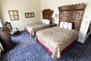 Habitación de hotel con dos camas, cabecero de madera, alfombra estampada y una mesita con lámpara.