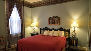 Un dormitorio con una cama grande, dos mesitas de noche con lámparas, un espejo decorativo y una alfombra estampada.