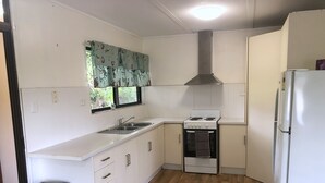 A compact kitchen with white cabinets, a stove, a sink, and a refrigerator. - Space and tranquillity at Red Door Cottage (Cooktown)