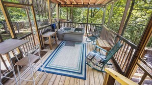 Une terrasse extérieure couverte, dotée d’un jacuzzi, de sièges et offrant une vue sur la forêt.