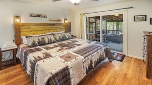 Une chambre à coucher avec une tête de lit en bois, un grand lit recouvert d’une couette aux motifs forestiers, une table de chevet et une vue sur une terrasse extérieure, accessible par une porte-fenêtre coulissante.