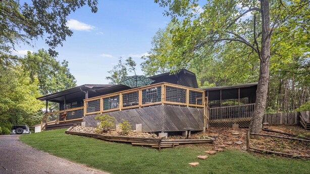 Une cabane en bois à deux étages, dotée d’une terrasse et entourée d’une pelouse bien entretenue et d’arbres.