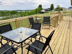 Une terrasse en bois avec une table et des chaises, donnant sur une étendue d’eau et une zone résidentielle.