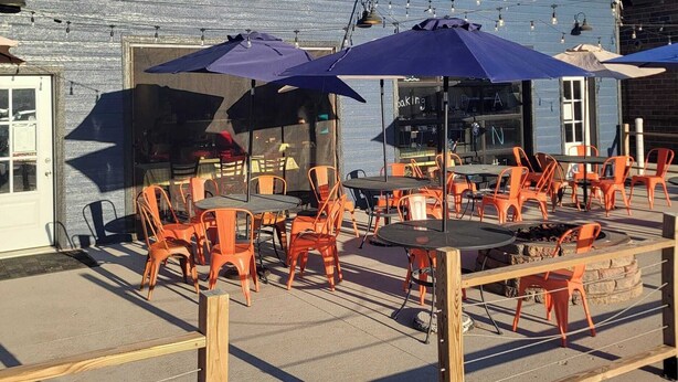 Een terras met oranje stoelen en paarse parasols voor een gebouw met een bord waarop staat: RISE & GRIND BAKERY AND KITCHEN.