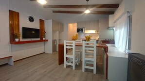 A compact kitchen with white cabinets, a wooden countertop, and a dining area with white chairs. - Casa del Condor (San Carlos de Bariloche)