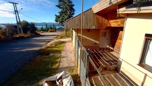 A wooden building with a porch, a paved driveway, and a view of a lake and mountains in the background. - Casa del Condor (San Carlos de Bariloche)