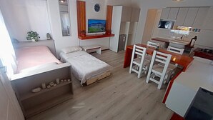 A compact living space with a bed, a small desk, a TV, and a kitchenette. - Casa del Condor (San Carlos de Bariloche)