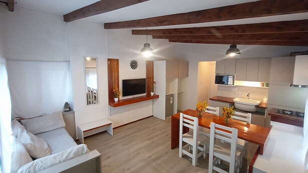 A compact kitchen with a dining area, a sofa, and a TV mounted on the wall. - Casa del Condor (San Carlos de Bariloche)