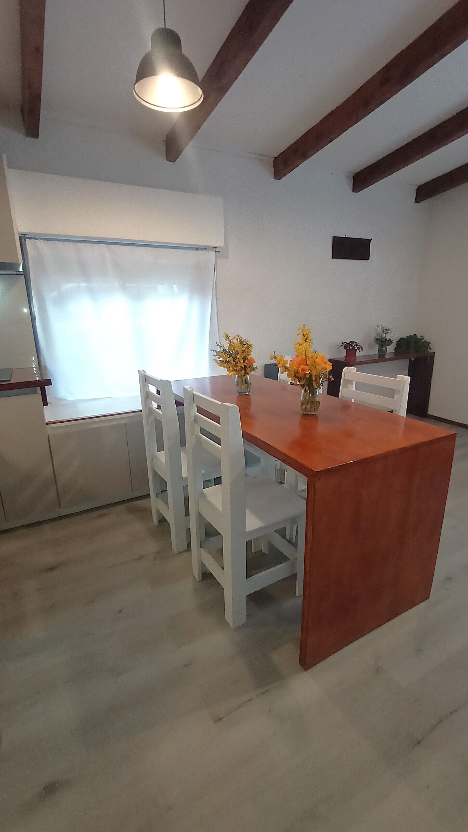 Un comedor con una mesa de madera, sillas blancas y dos jarrones de flores.