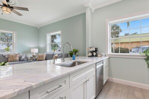 A kitchen with a marble countertop, white cabinets, a built-in dishwasher, and a window with a view of the outside.