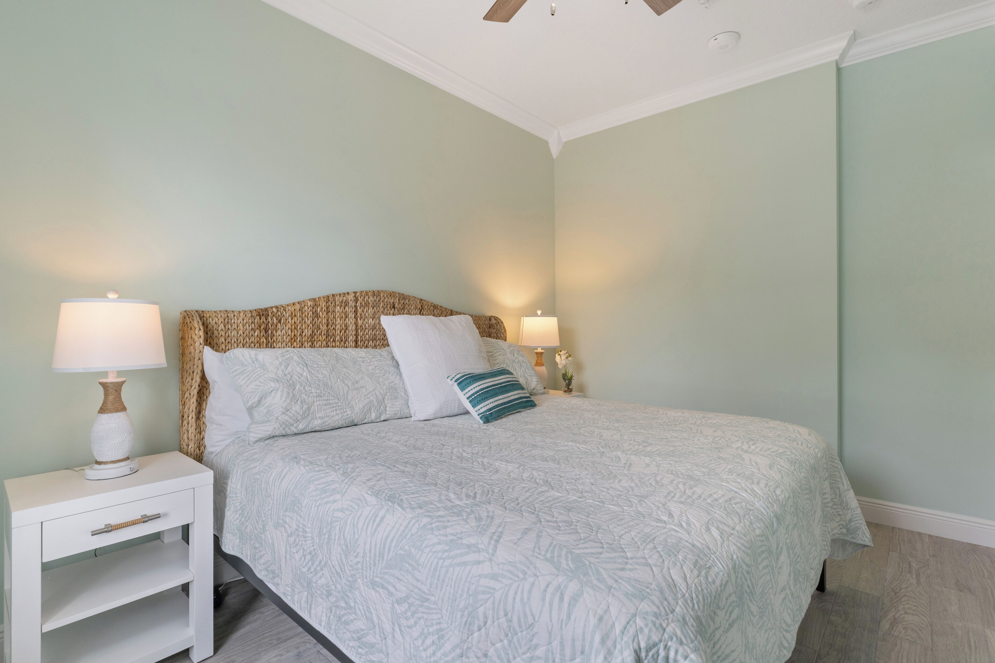 A bedroom with a bed, two bedside tables with lamps, a wooden headboard, and a light green wall.